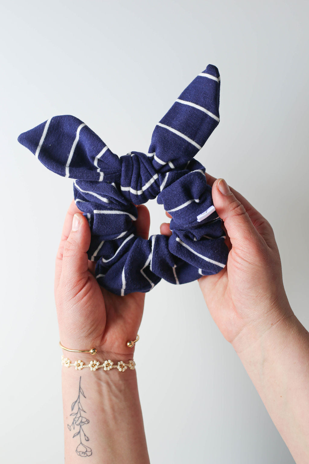 Navy blue scrunchie with white stripes held by a person against a light gray background