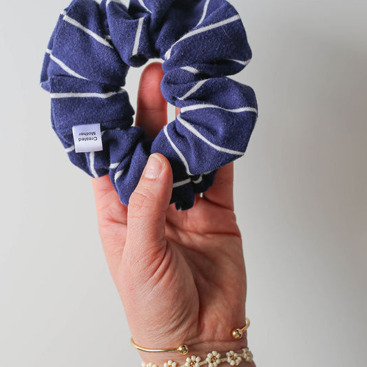 Navy blue scrunchie with white stripes held by a hand against a light gray background