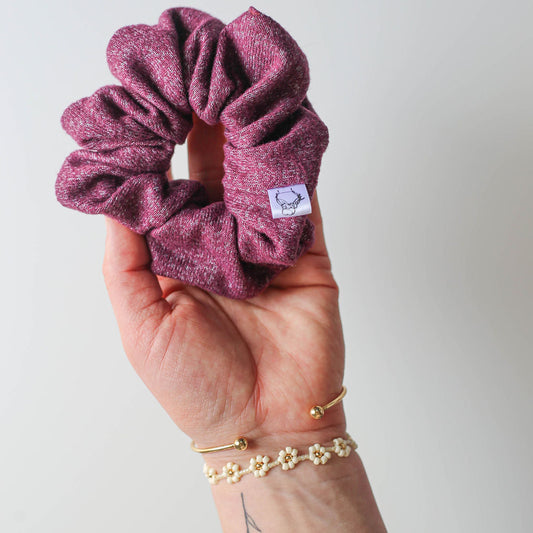 Plum heather scrunchie held in tattooed hand with bracelet