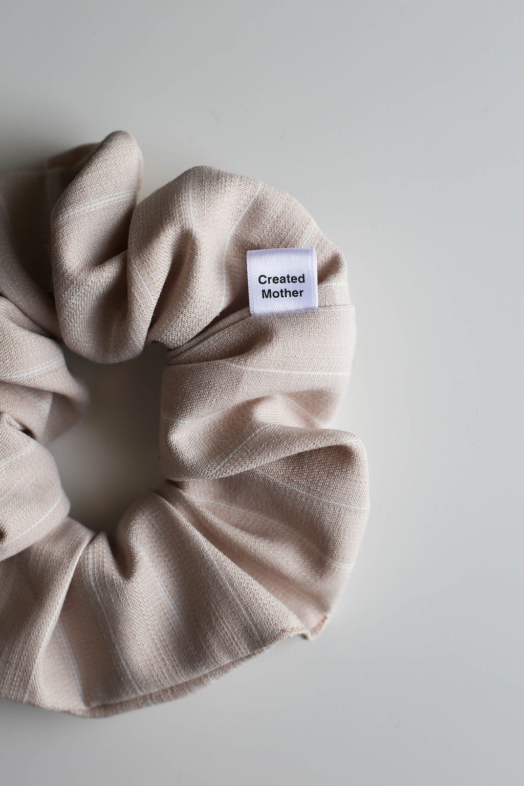 Beige all-day-hold scrunchie with a label on a light gray background