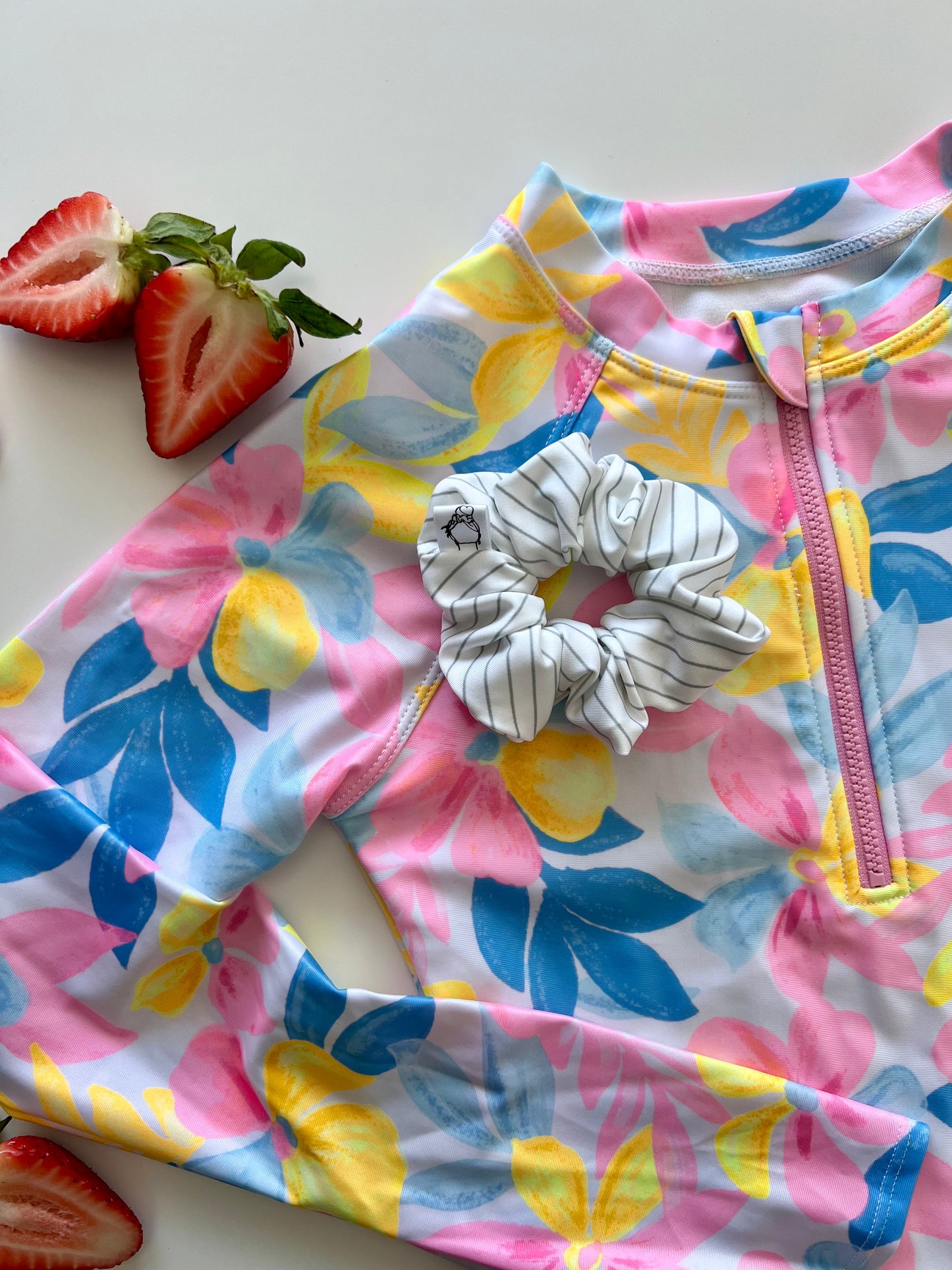Colorful children's swimsuit with floral pattern and a scrunchie on a white surface.