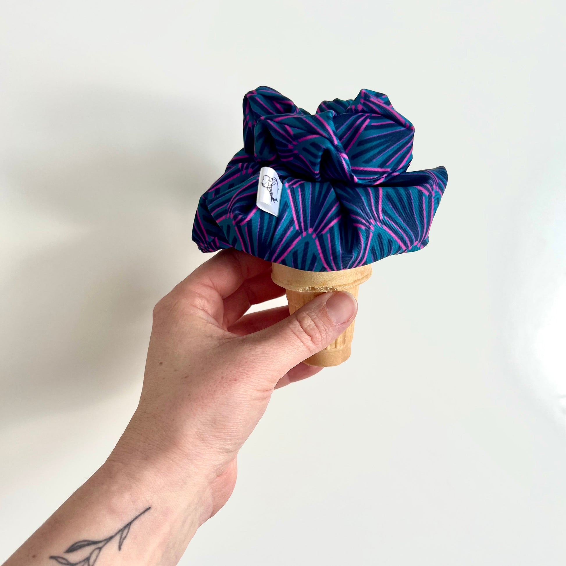 Hand holding an ice cream cone with two colourful scrunchies on top as ice cream  against a white background