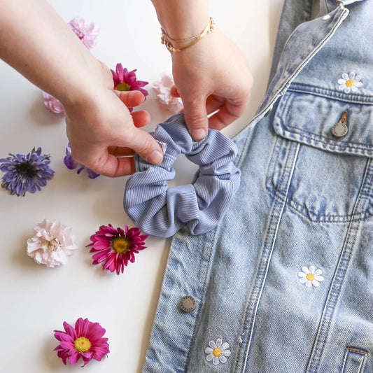 Person holding a blue scrunchie with flowers and a denim jacket in the background