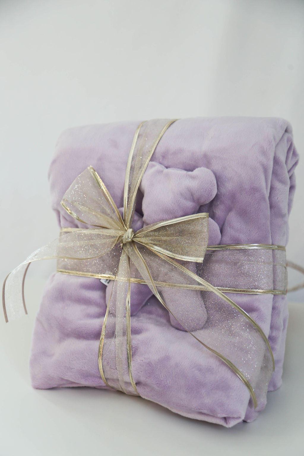 Purple plush blanket and matching comfort bear with a gold bow on a white background