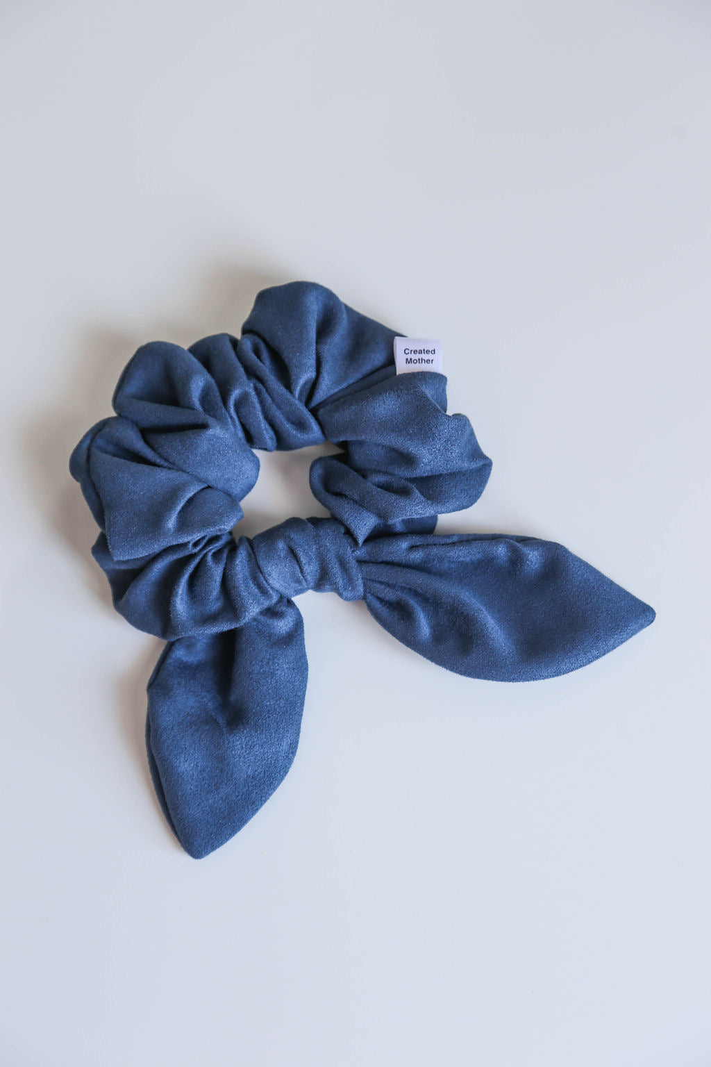 Elegant suede scrunchie in shadow blue, offering a secure hold and versatile style for every look.