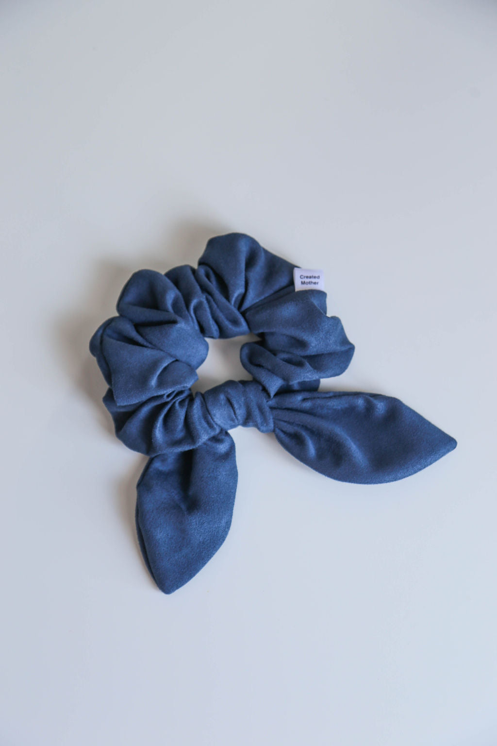 A soft, ocean blue suede scrunchie with a smooth texture, handmade for all-day comfort and hold.