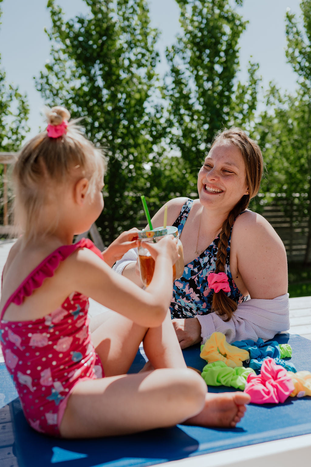 Woman and child sitting at a table outdoors with colorful SWIM Scrunchies