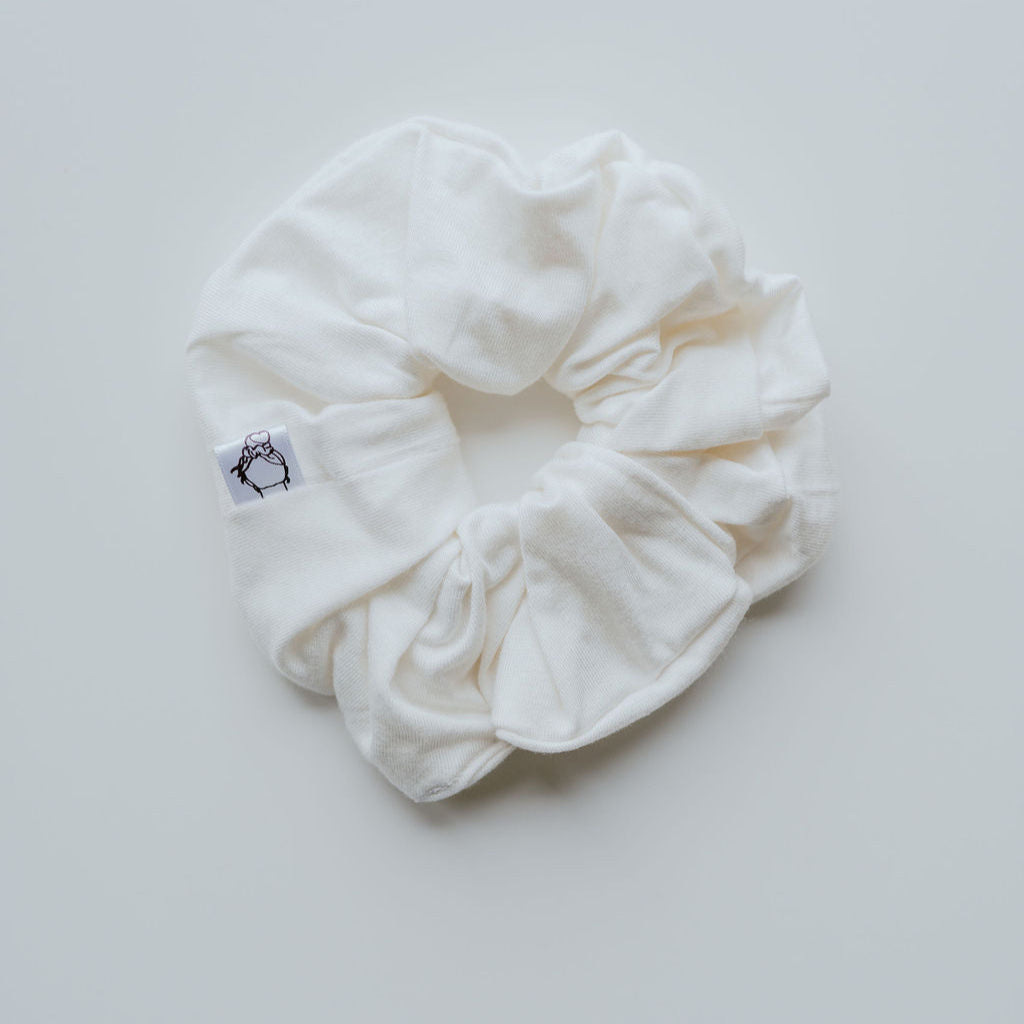White scrunchie with a brand logo on a light gray background