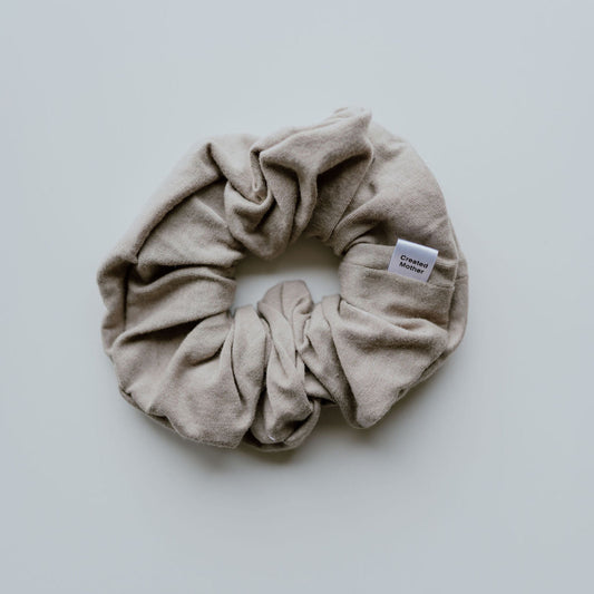 Beige scrunchie with a brand label on a light gray background