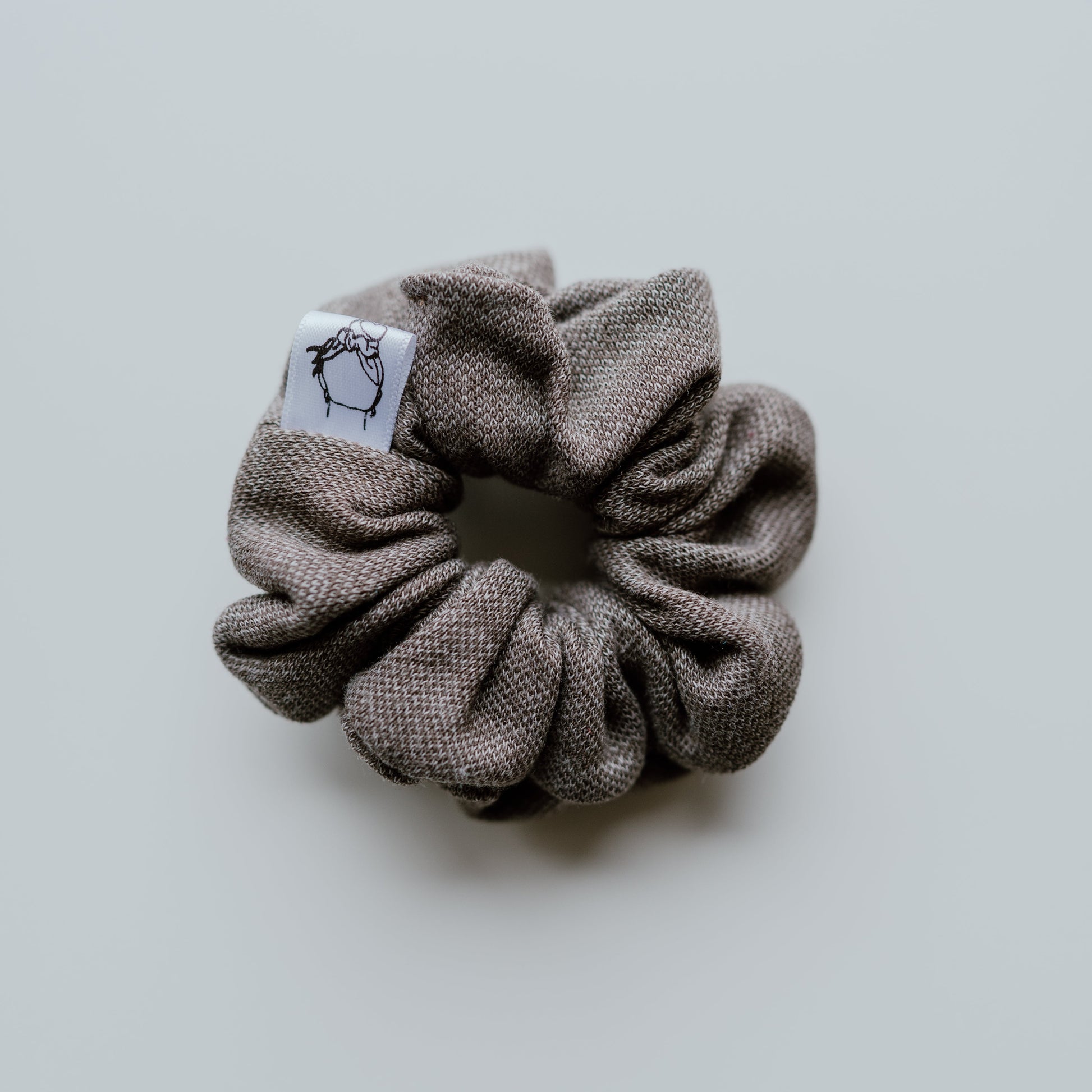 Gray scrunchie with a brand label on a light gray background