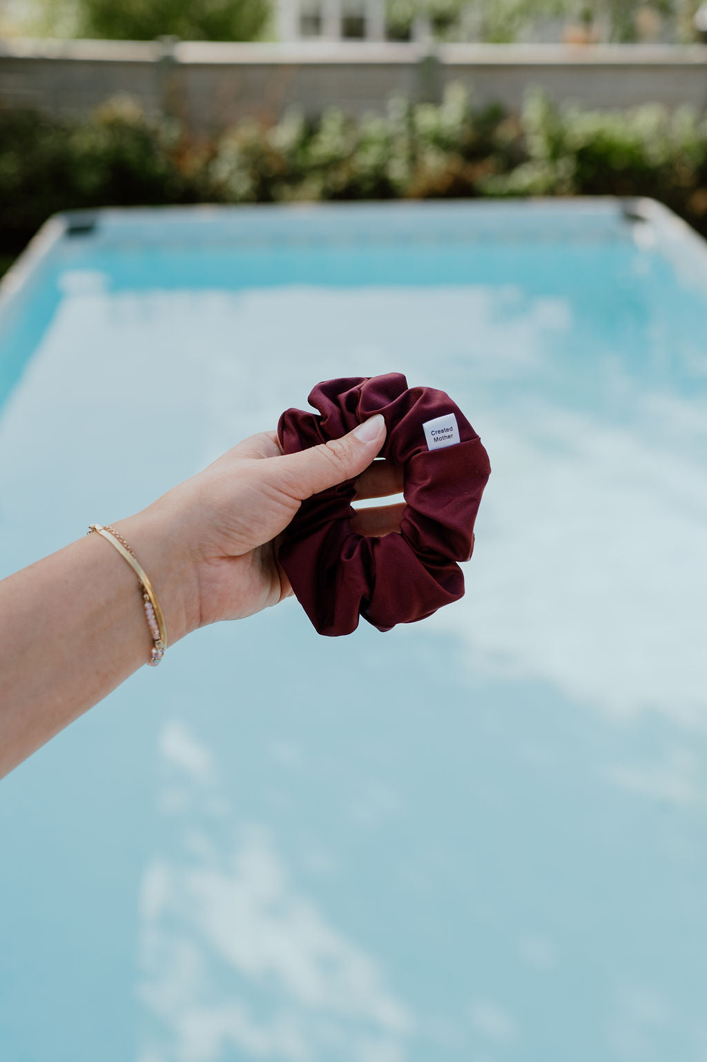 Hand holding a burgundy scrunchie with a pool in the background